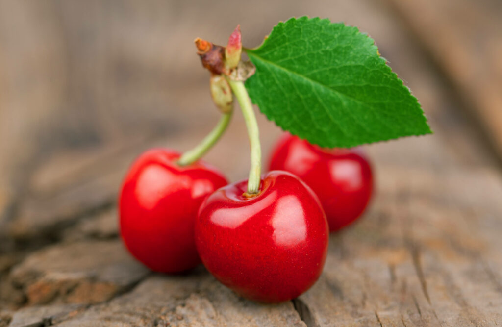 Glossy red cherries with green leaf on rustic wooden background vibrant high-resolution wallpaper