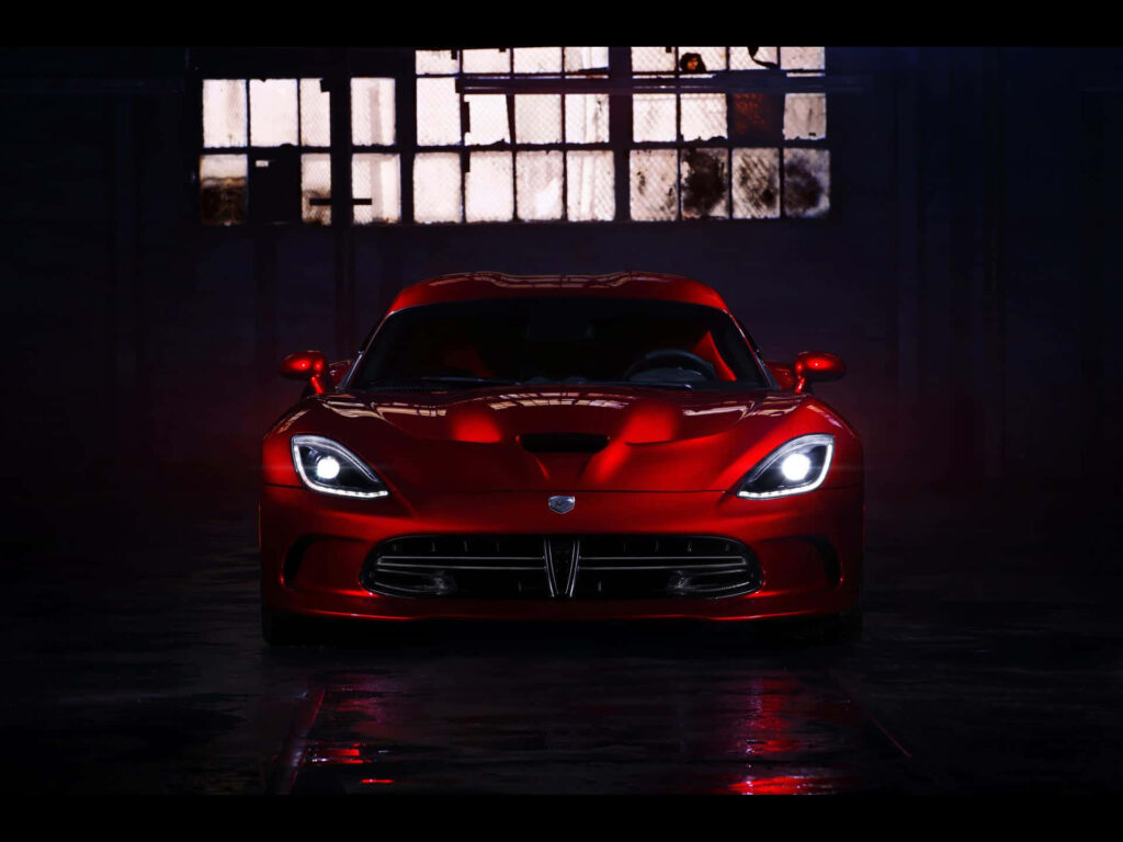 Glossy red Dodge Viper in dim warehouse with headlights on dramatic powerful automotive wallpaper