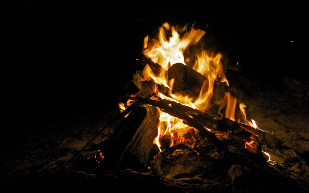 Glowing campfire with bright orange flames lighting rustic logs in a cozy outdoor night scene Wallpaper