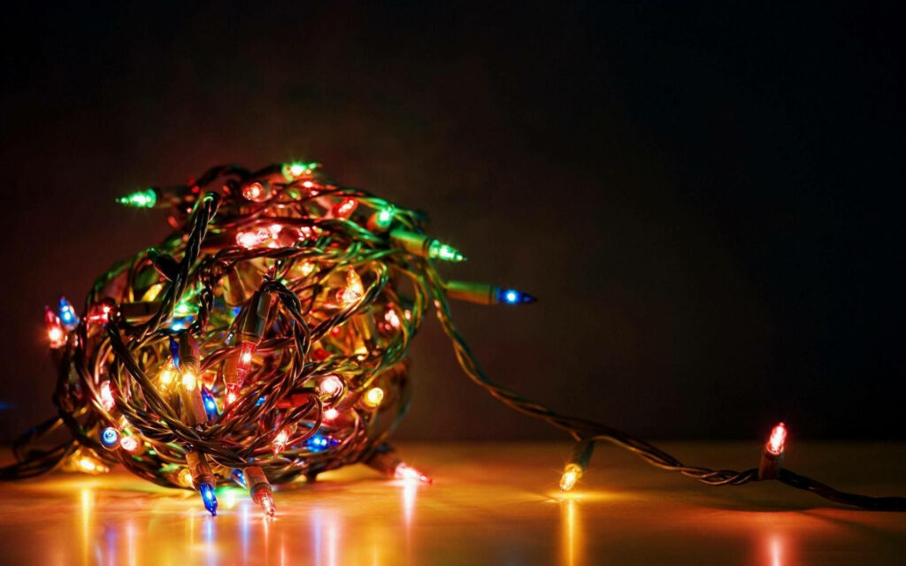 Festive Fantasia: Colorful Christmas Lights Cascade on Wooden Flooring Amidst a Mysterious Backdrop Wallpaper