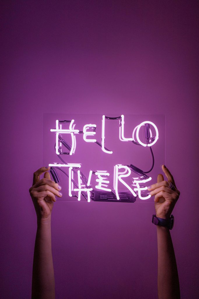 Two hands hold glowing Hello There neon sign on deep purple background minimalist wallpaper