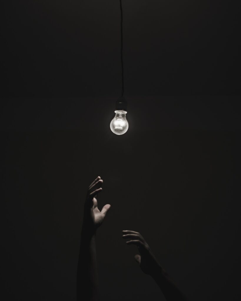 Reaching for Light: Dark Room with Glowing Bulb Wallpaper Background