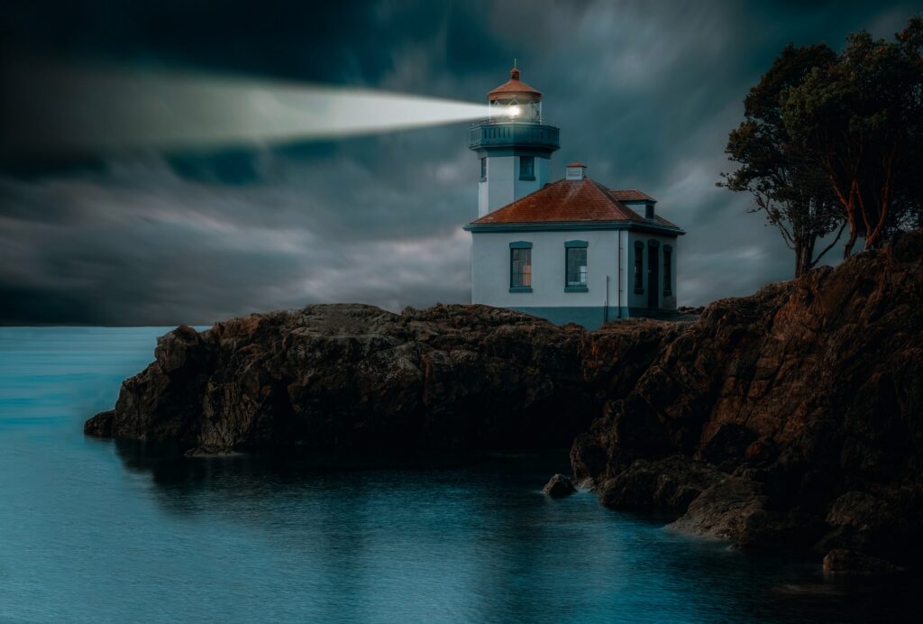 Glowing lighthouse on rocky cliffs shining over calm night ocean with dramatic blue clouds wallpaper
