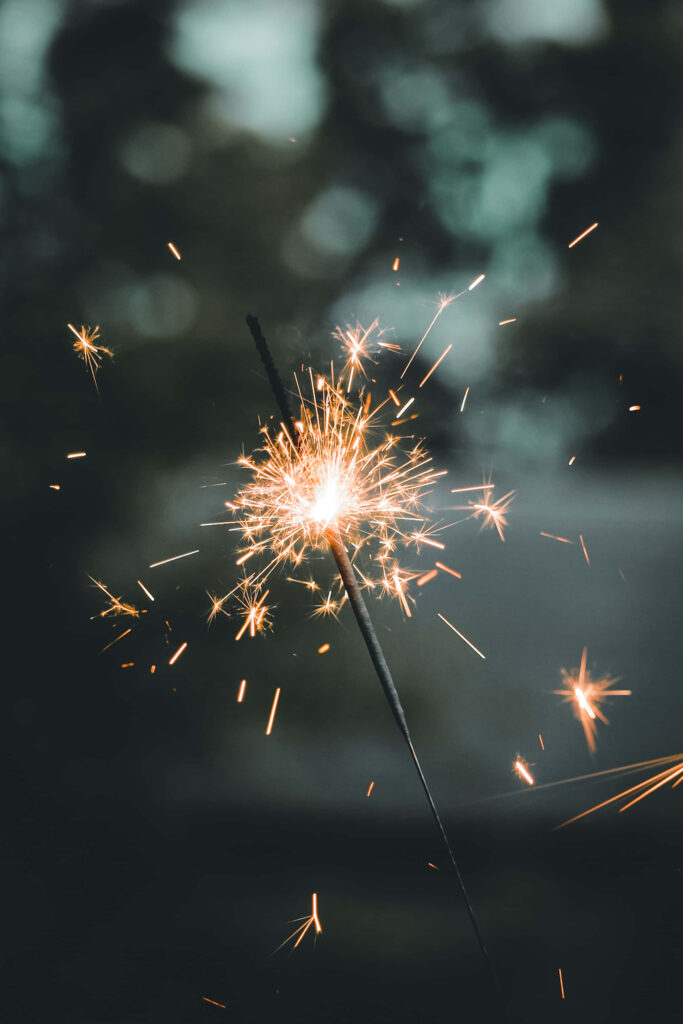 Glowing orange sparkler igniting bright sparks against dark blurred background festive light Wallpaper