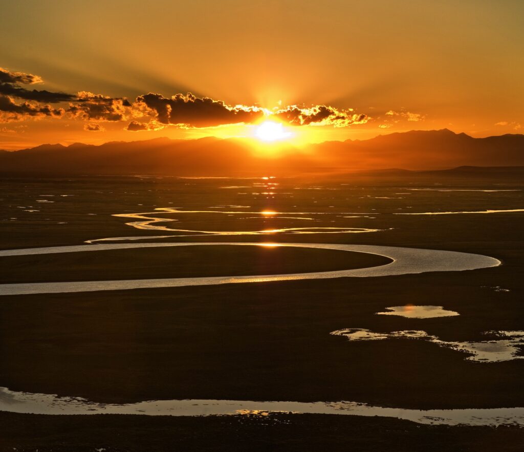 Glowing orange sunset over scenic river bends with reflective pools and vibrant warm sky clouds Wallpaper