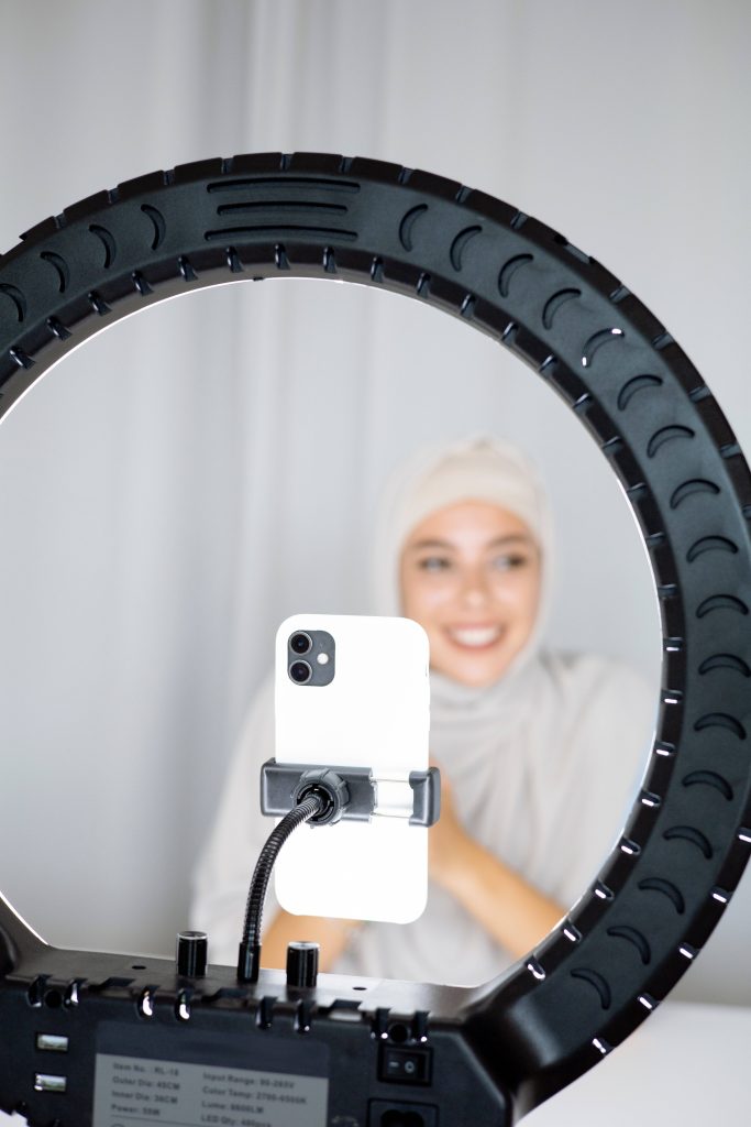 White smartphone with glowing ring light and blurred smiling woman in hijab wallpaper background
