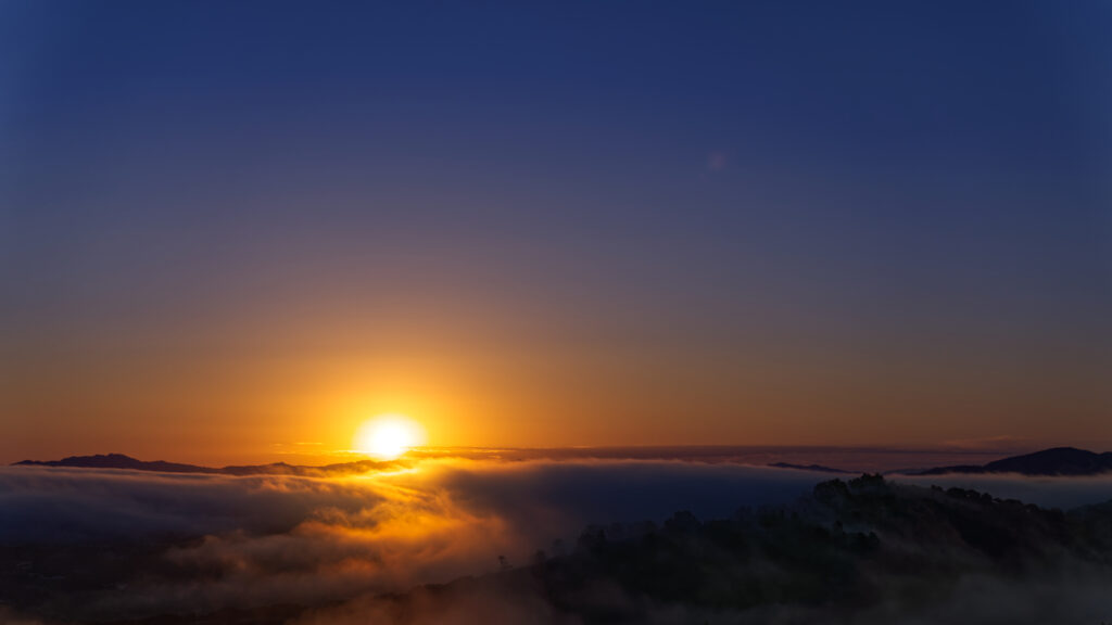 Glowing sunset over misty mountains with orange sky and dramatic clouds at horizon wallpaper