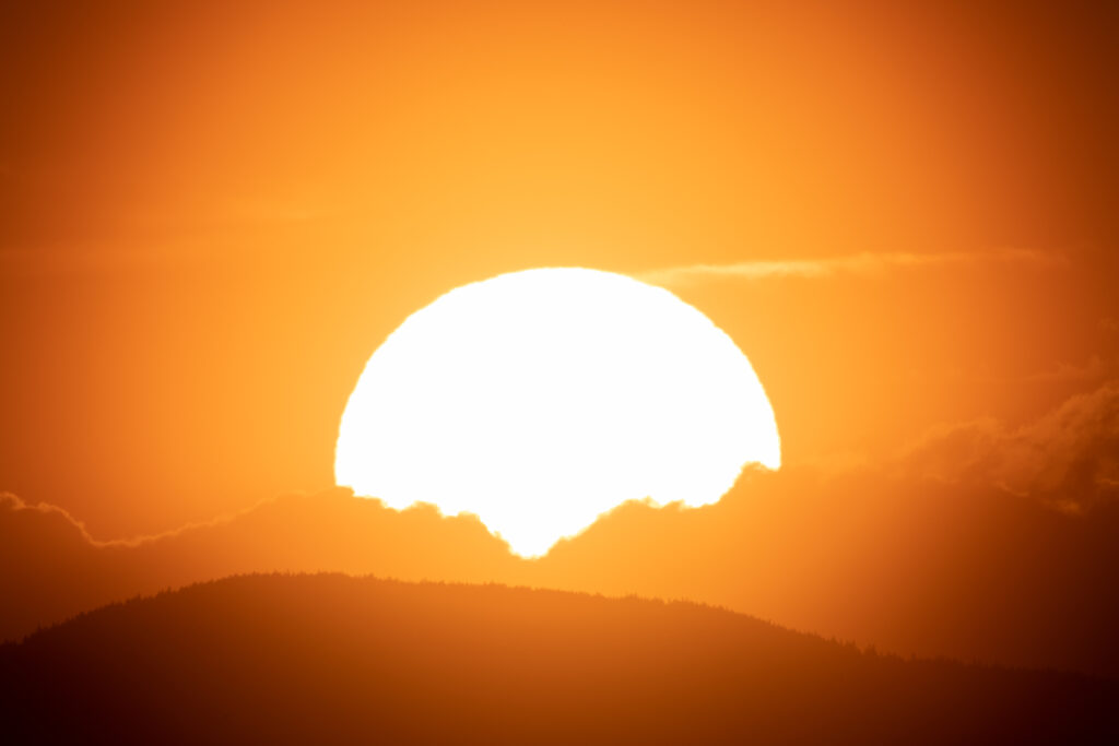 Glowing sun setting behind rolling hills with dramatic silhouettes warm orange yellow sky wallpaper