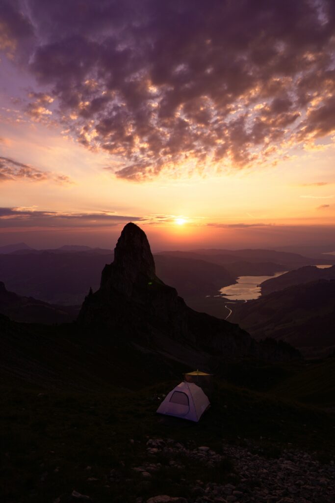 Vibrant wallpaper of glowing sunset over rugged mountains with solitary tent camping scene