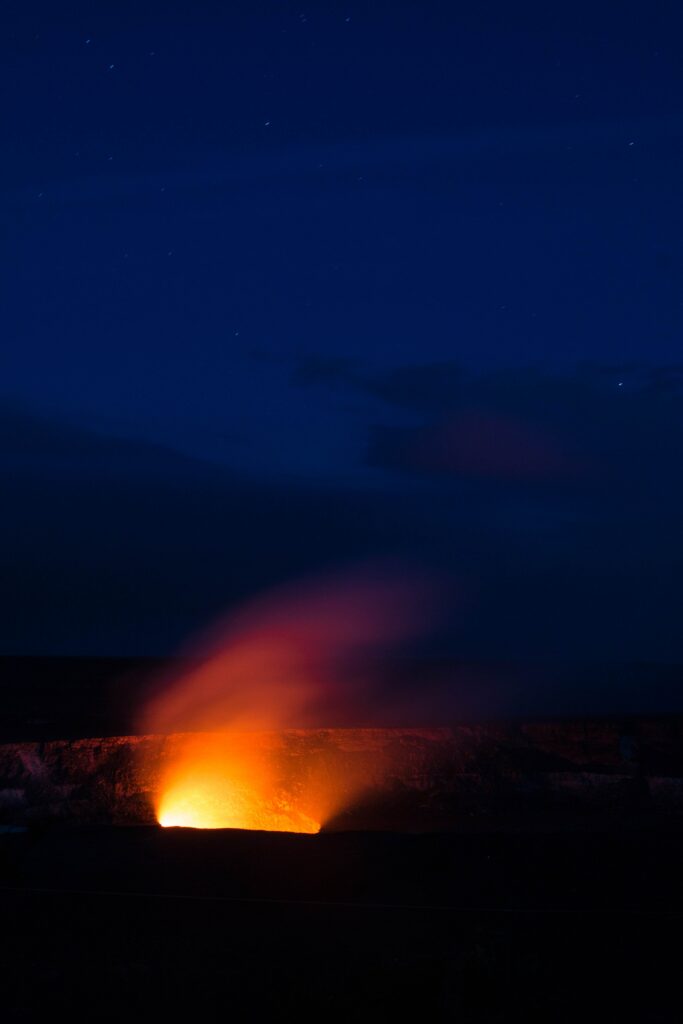 Glowing erupting volcano at night with fiery lava against starry deep blue sky wallpaper background