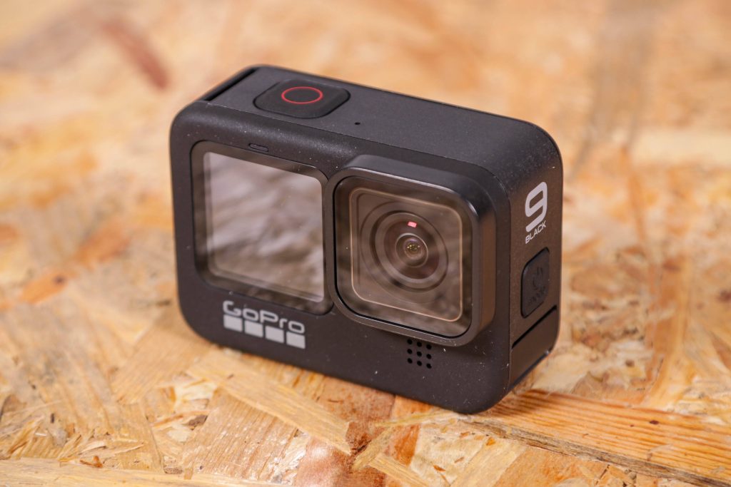 GoPro HERO9 Black action camera on textured OSB wood surface showing front display and lens Wallpaper