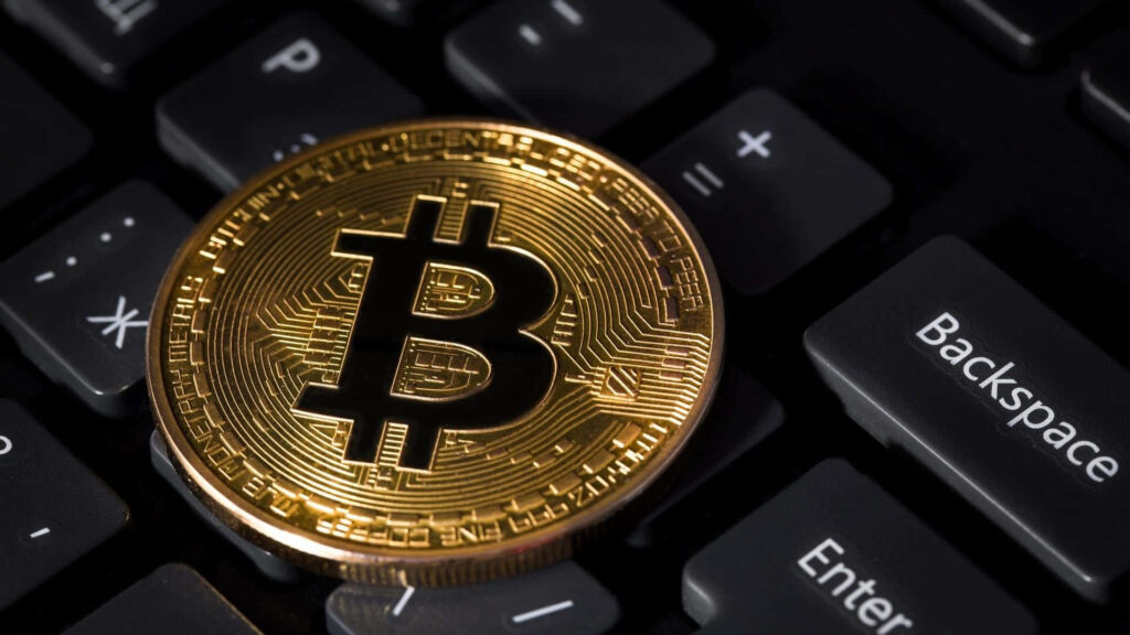 Gold Bitcoin coin on black keyboard depicting digital currency and modern technology wallpaper