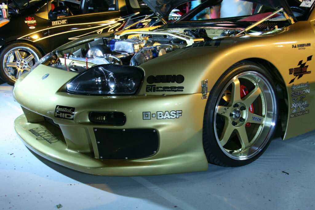 Gold JDM car with custom wheels and exposed engine under bright lights automotive wallpaper background
