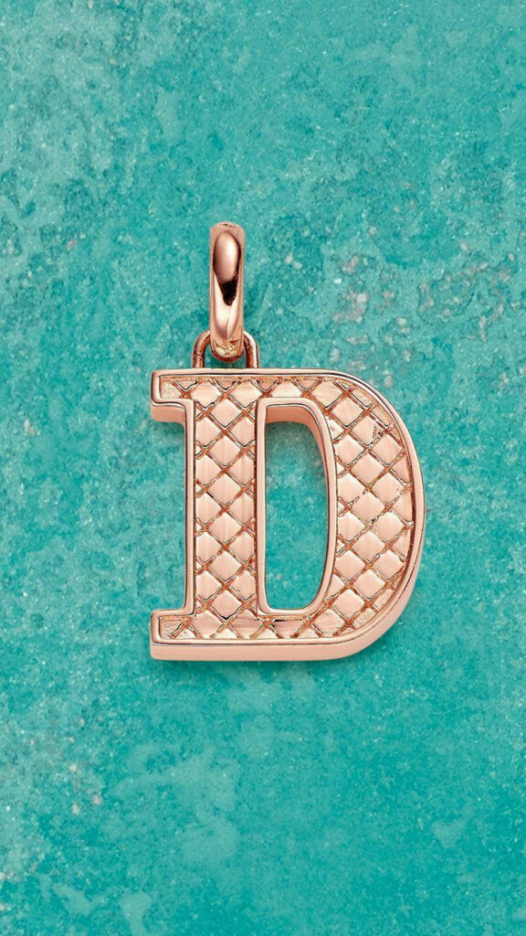 Gold letter D pendant with quilted texture on vibrant turquoise modern wallpaper background