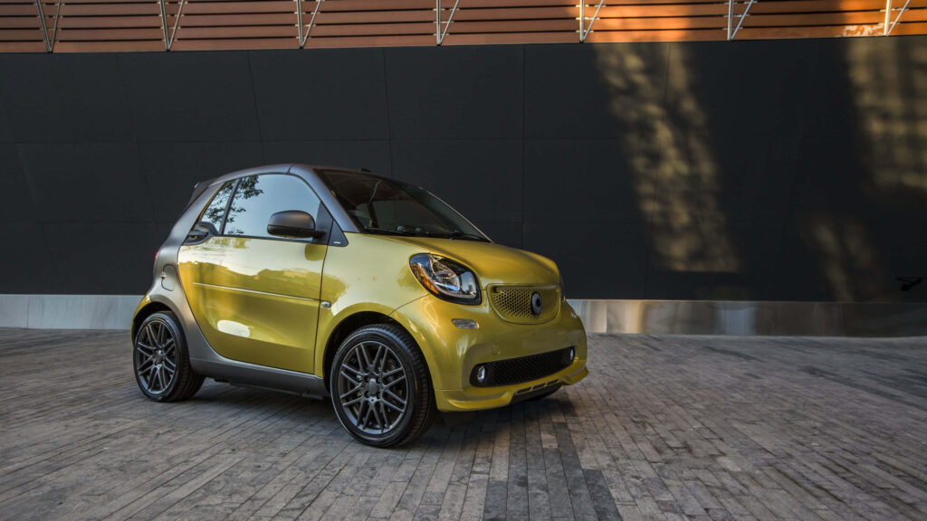 Gold Smart Fortwo compact car with sporty alloy wheels parked on modern urban stone pavement Wallpaper