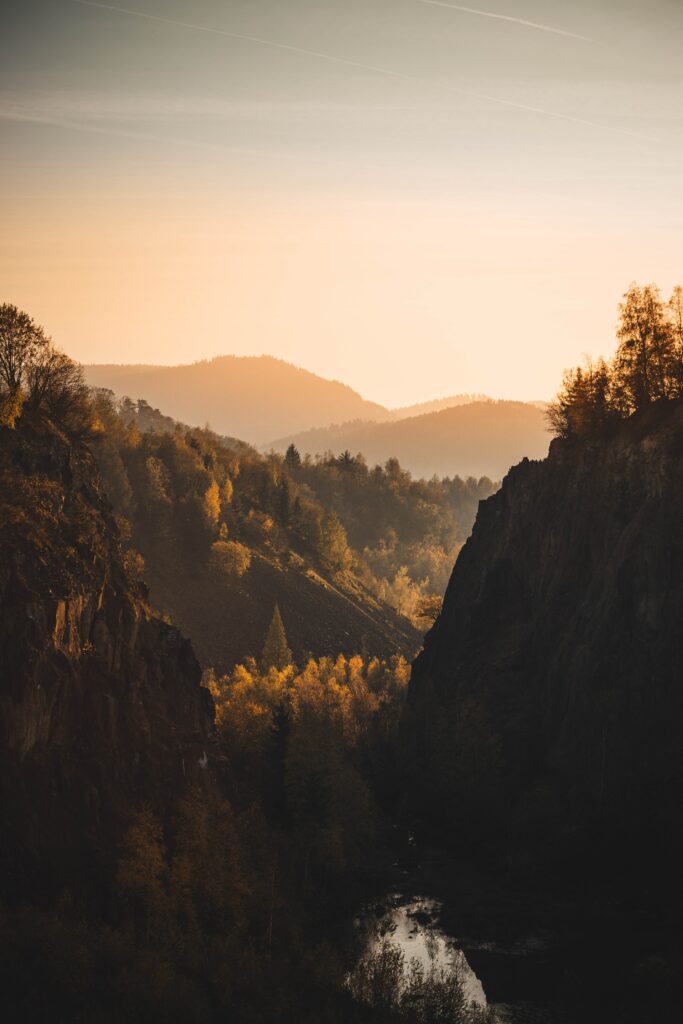 Serene autumn landscape with rugged rocks tree-covered hills golden sunlight and distant mountains Wallpaper