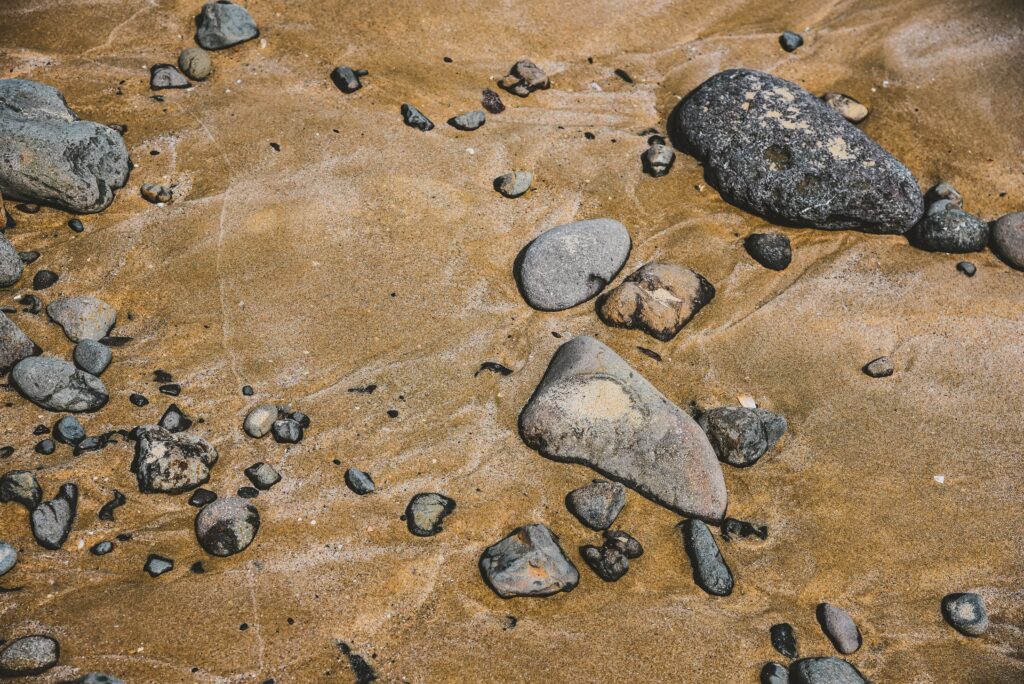 Natural stones and pebbles on golden beach sand textured wallpaper background serene coastal scene