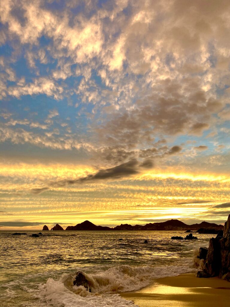 Golden beach with rugged cliffs and dramatic cloudy sky reflecting warm sunlight waves wallpaper