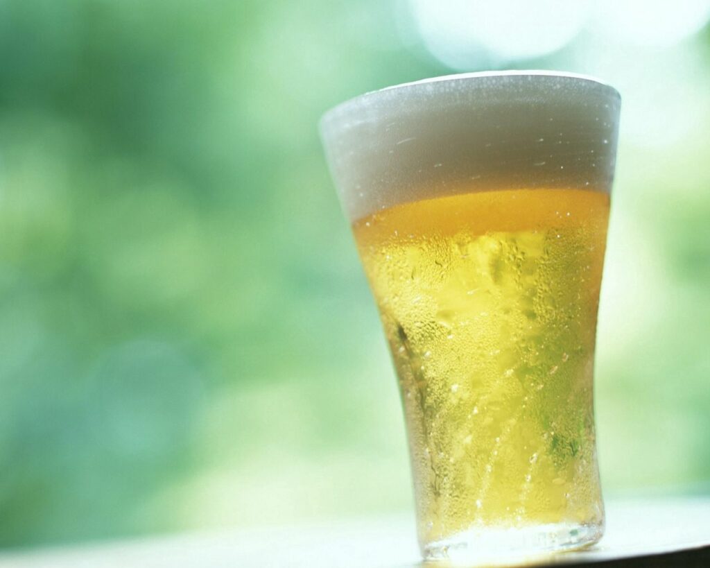 Golden-Hued Refreshing Beverage in Glass - Soft Green Wallpaper