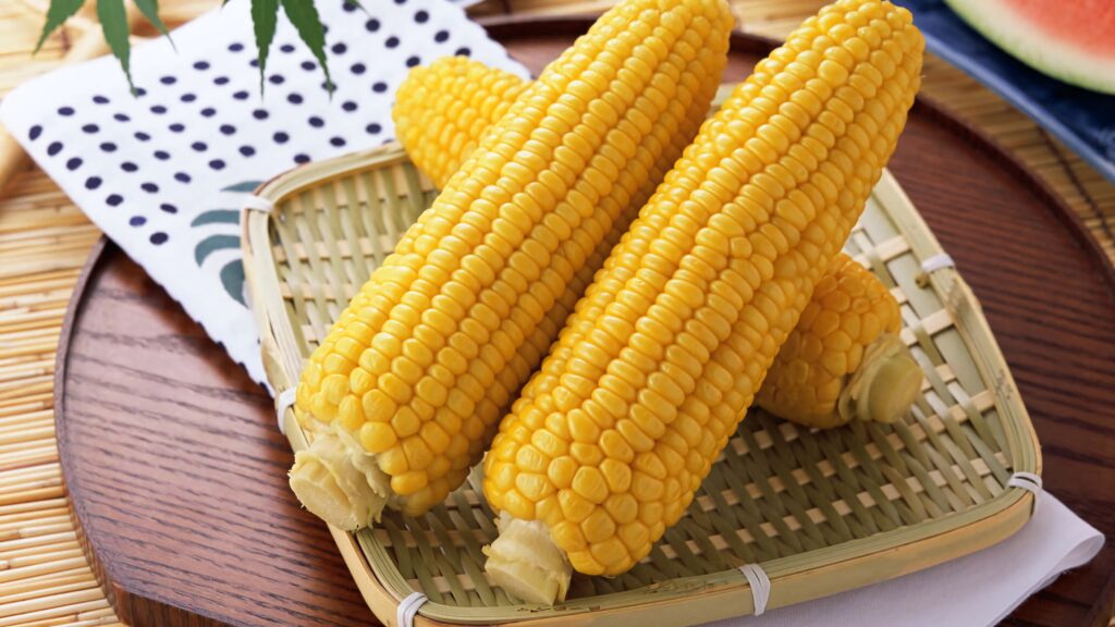 Freshly boiled golden corn cobs on bamboo tray with rustic textures food nature wallpaper background
