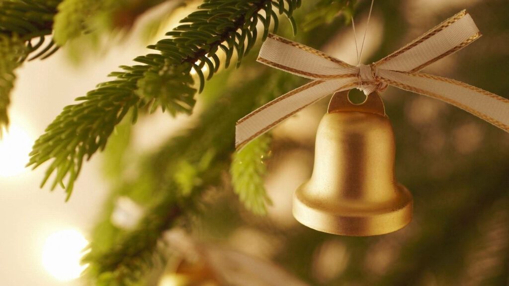 A Festive White Ribbon with Golden Borders Adorning a Cheerful Christmas Bell Against a Beautifully Lit Christmas Tree Background Wallpaper