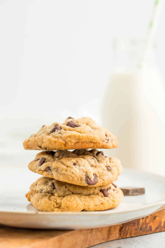 Freshly baked golden chocolate chip cookies stacked on a white plate with milk background Wallpaper