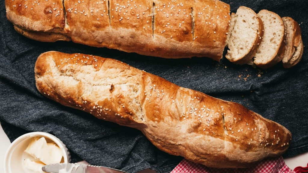 Two sesame seed baguettes on dark cloth showing soft airy texture fresh bread background Wallpaper