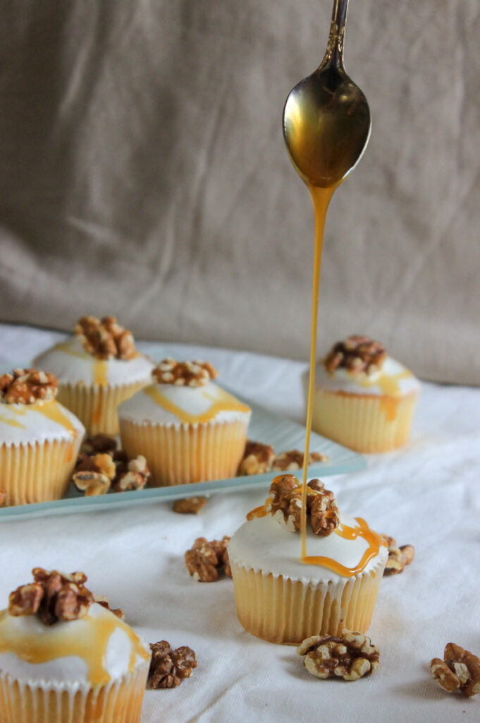 Vanilla cupcakes with white icing walnuts drizzled golden caramel cozy cream wallpaper background