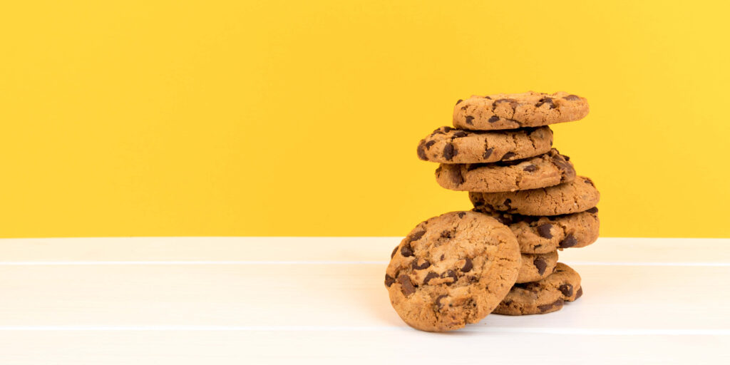 Stack of golden chocolate chip cookies on white wooden surface with bright yellow background Wallpaper
