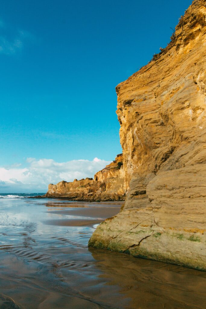 Golden cliffs towering over calm coastline with soft sand and gentle waves under clear sky Wallpaper
