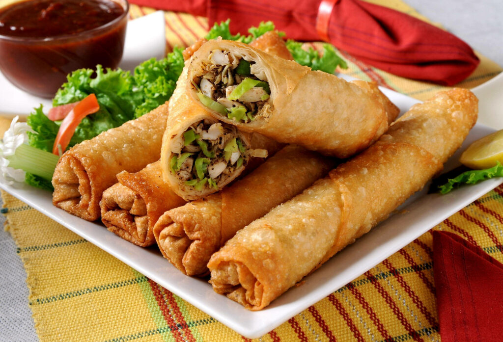 Golden crispy egg rolls sliced with fresh spring onions and dipping sauce on white plate wallpaper