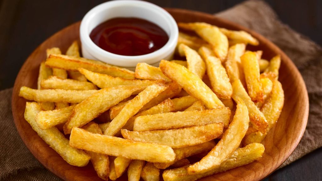 Golden crispy French fries on rustic wooden plate with ketchup in warm light background Wallpaper
