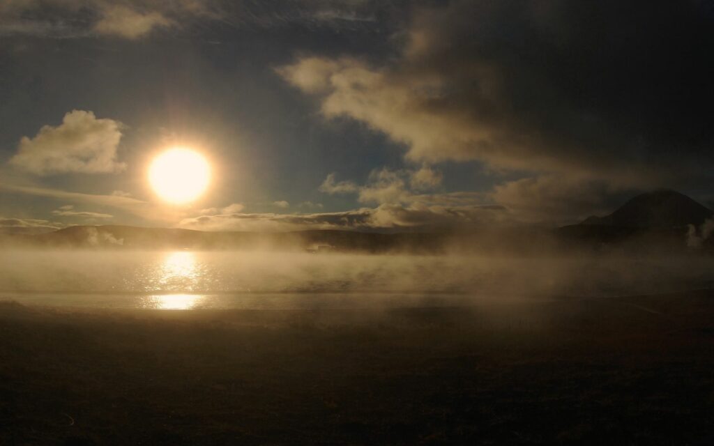 Stunning dawn wallpaper with sun rising over misty lake casting golden light and fog vapor