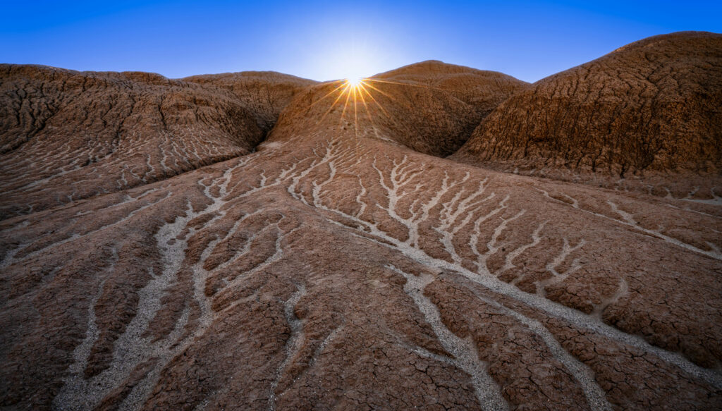 Dawn light on rugged hills with textured relief under vivid blue sky nature wallpaper background