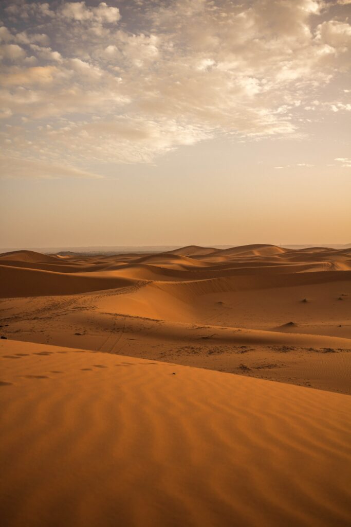 Vast desert landscape with golden sand dunes under warm sky and scattered clouds wallpaper background