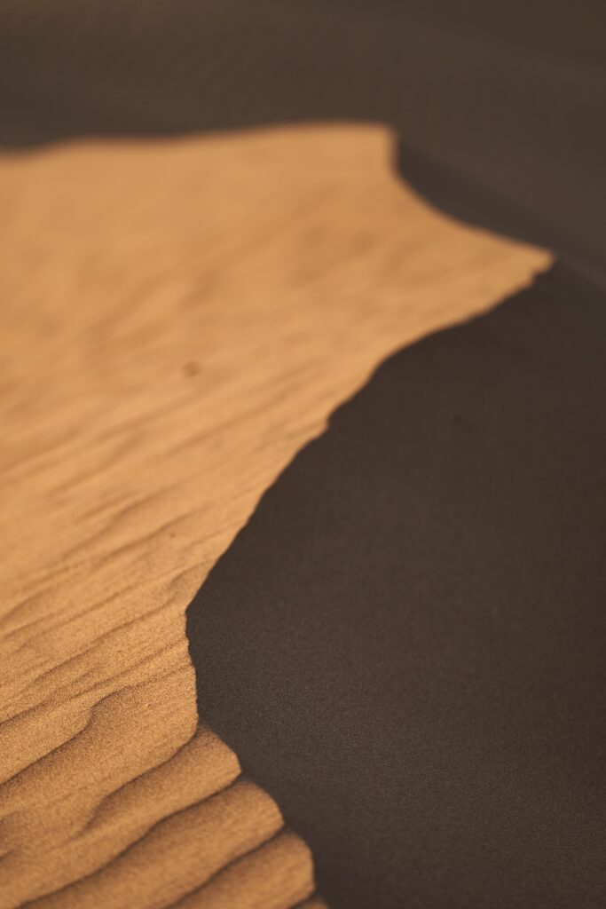 Minimalistic desert wallpaper with smooth golden sand dunes textured by deep shadowed ripples