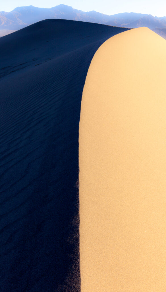Golden desert sand dunes with dramatic shadows and distant mountains under clear sky wallpaper