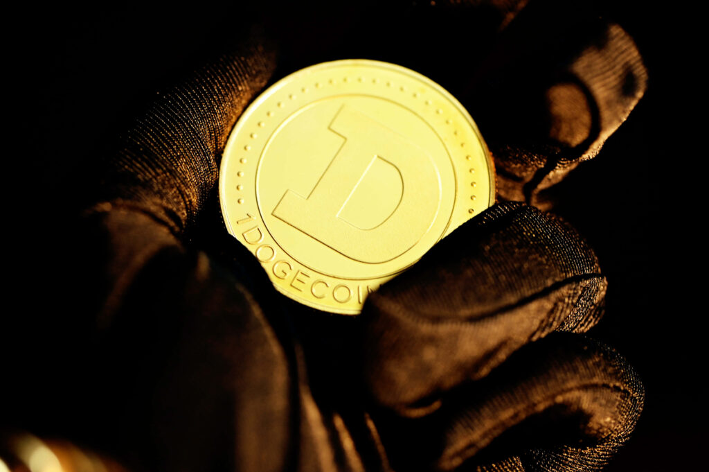 Gloved hand holding shiny golden Dogecoin with embossed logo and detailed rim on dark tech background Wallpaper