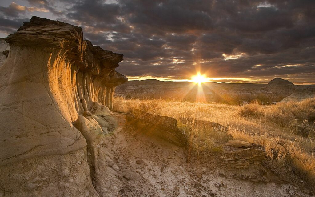 Dramatic desert canyon sunset with rugged stone formations and golden dry grasses wallpaper