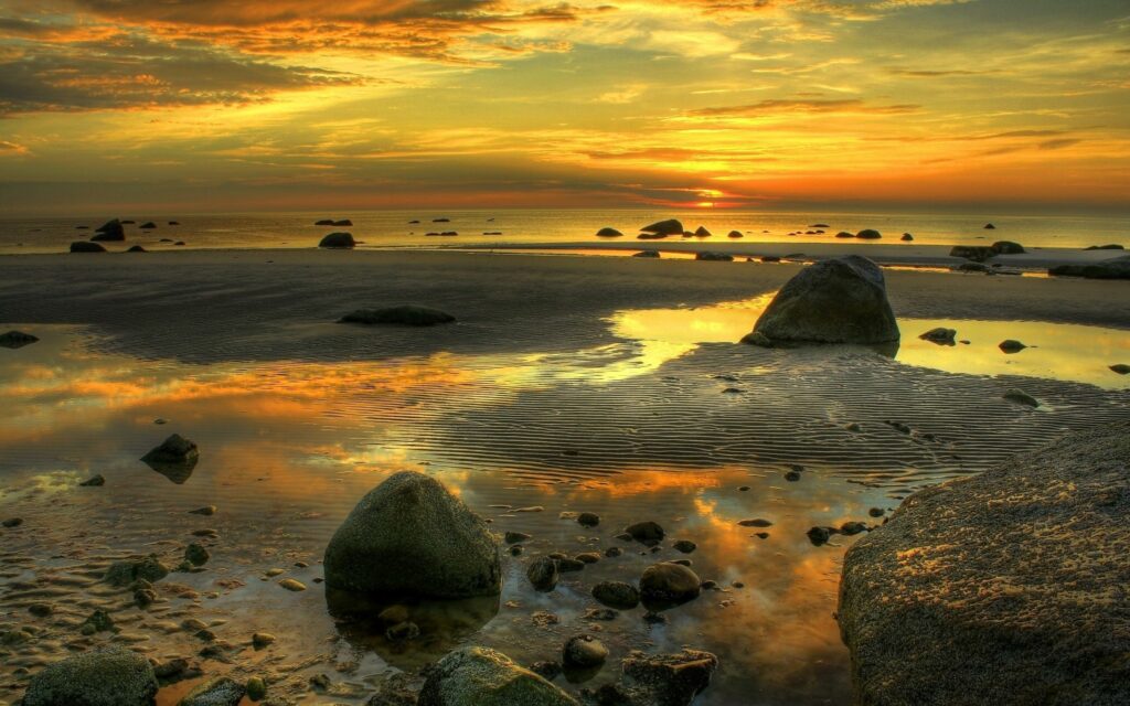 Golden evening sunlight on serene seashore with stones and reflective calm sea ripples wallpaper
