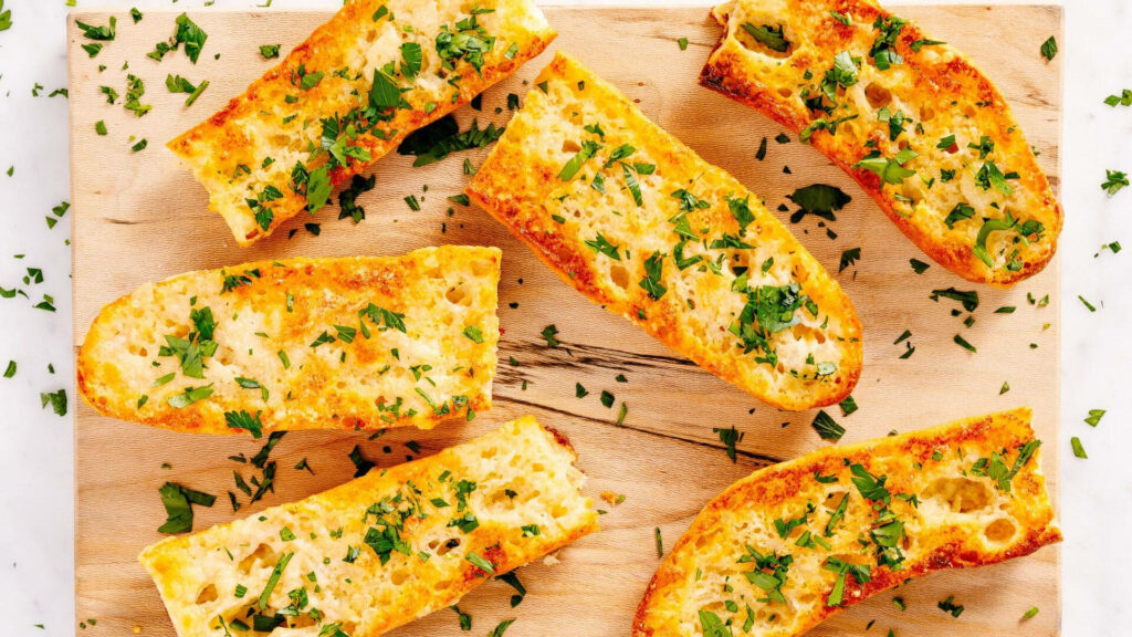 Golden garlic bread with melted butter minced garlic and parsley on rustic wooden board background Wallpaper