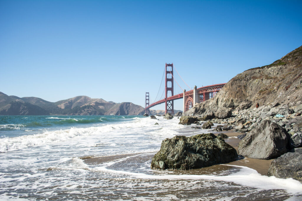 Golden Gate Bridge over rugged coast with rolling waves and clear blue sky wallpaper background