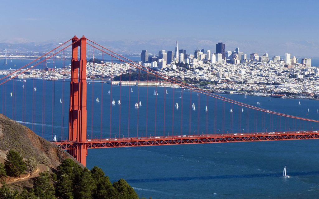 Golden Gate Bridge arching over San Francisco Bay with sailboats and city skyline in daylight Wallpaper