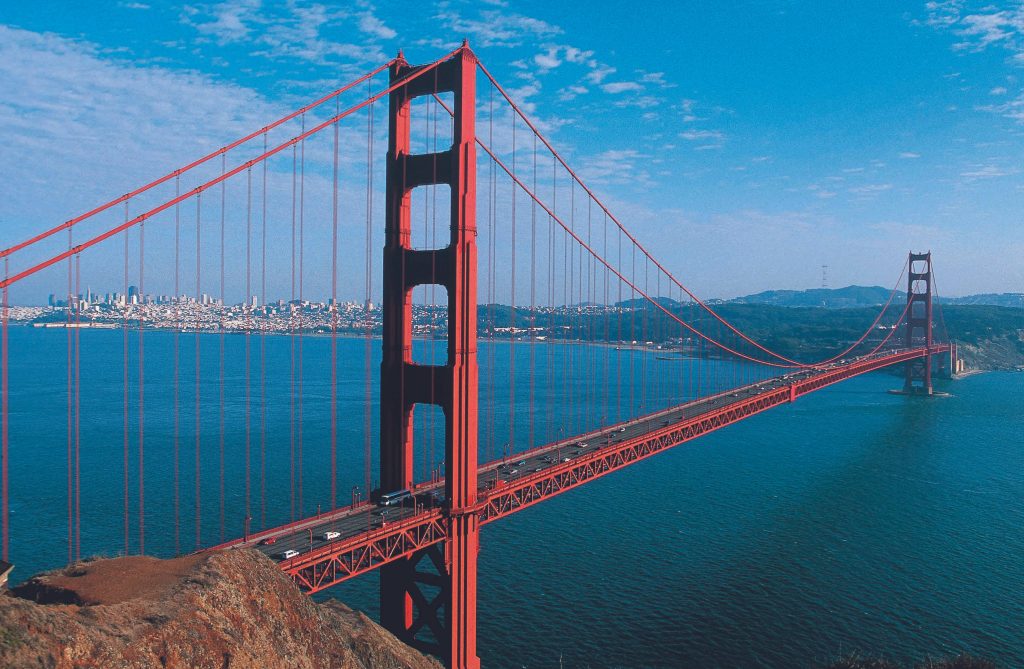 Aerial view of Golden Gate Bridge International Orange spanning blue waters with San Francisco skyline Wallpaper