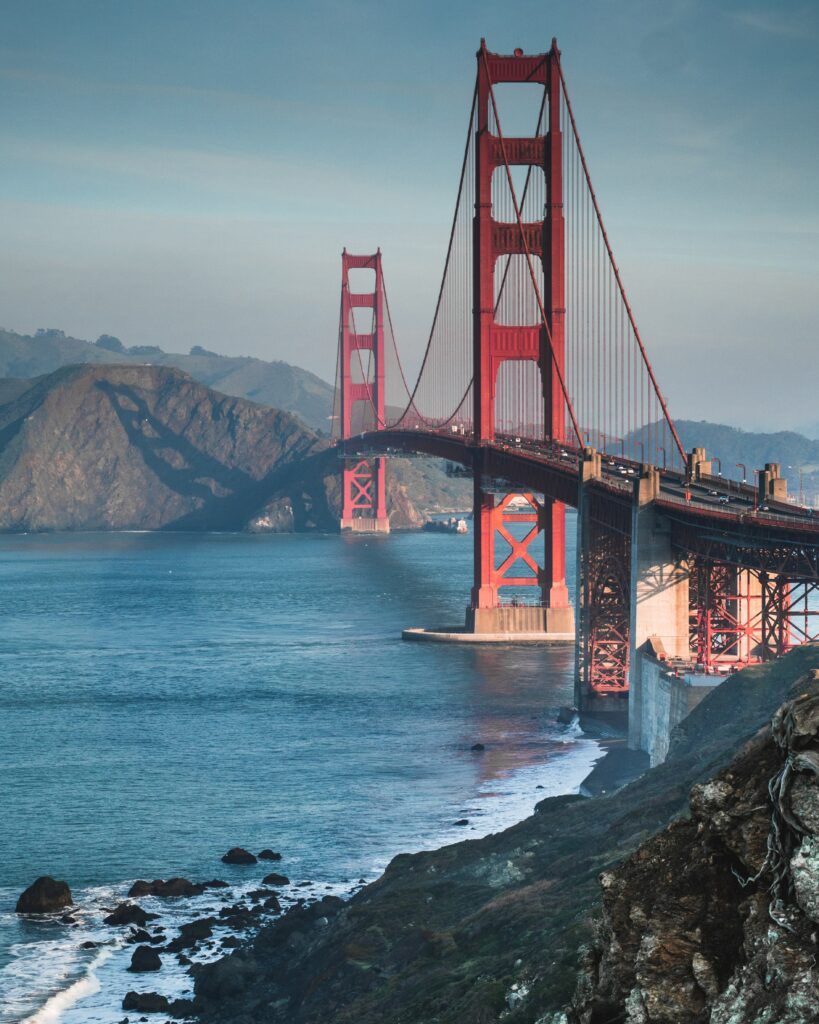 Golden Gate Bridge red architecture over blue sea with coastal rocks and distant hills wallpaper