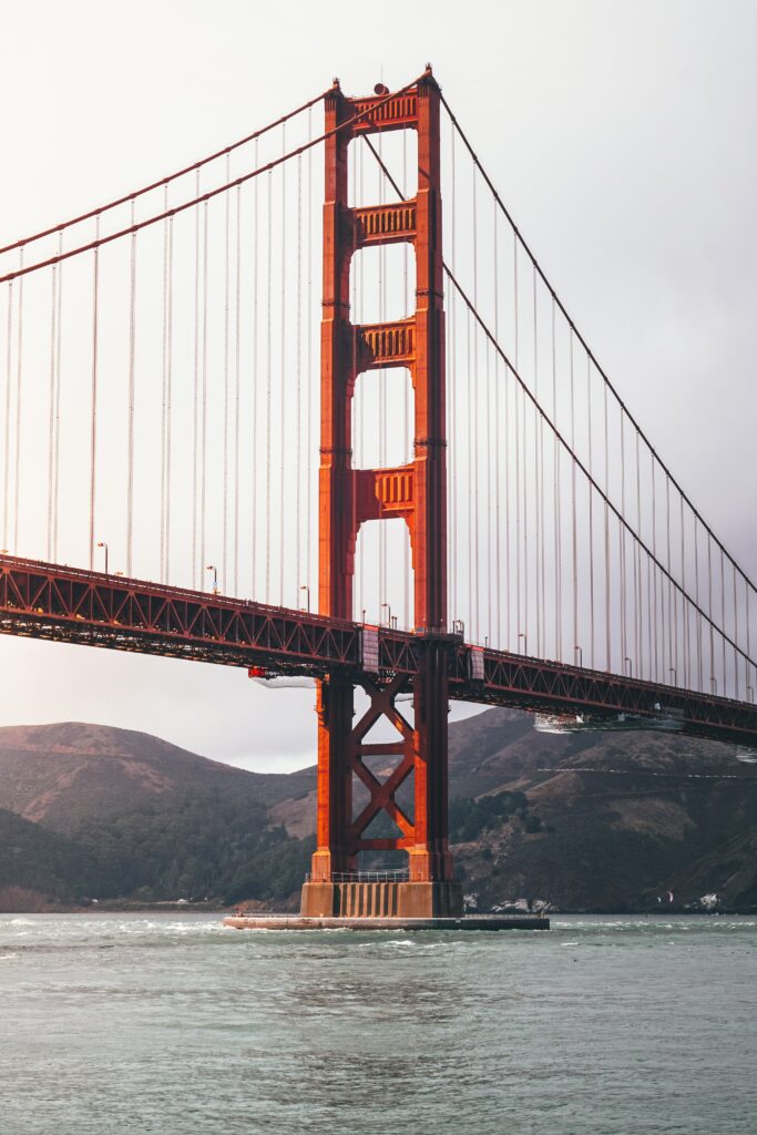Golden Gate Bridge red architecture over calm sea with green hills and soft overcast sky wallpaper