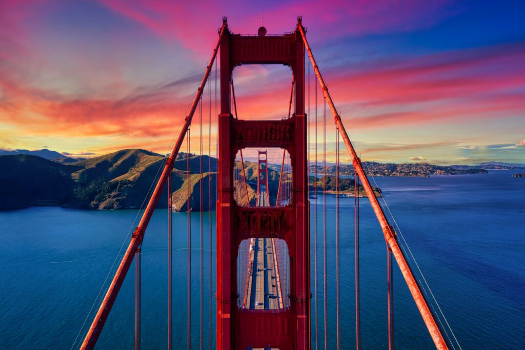 Vibrant wallpaper of iconic red bridge over blue water with green mountains and colorful sunset sky