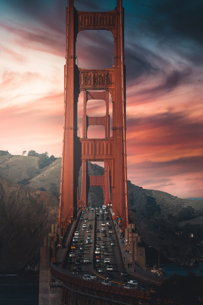 Golden Gate Bridge at sunset with vibrant sky cars driving and mountains in the background Wallpaper