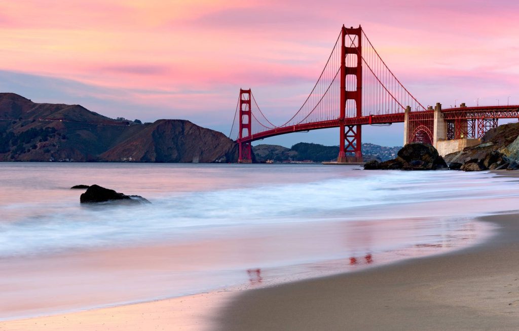 Golden Gate Bridge at sunset with pink sky and calm waves on sandy beach wallpaper background