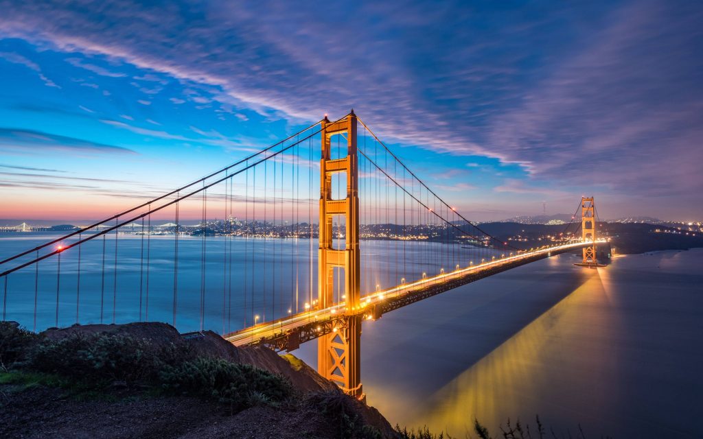 Golden Gate Bridge at twilight with glowing amber lights and deep blue sunset sky over bay Wallpaper